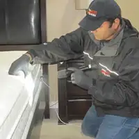 Bed bug inspection technician checking a mattress and bed frame for signs of infestation in Arlington, TX