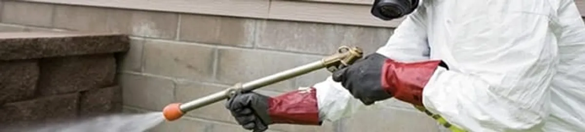 Pest control technician applying exterior insect treatment along a home foundation in Arlington, TX