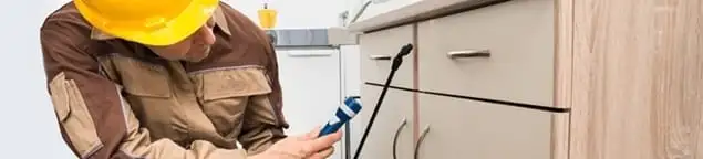 Roach exterminator applying treatment under kitchen cabinets in Arlington, TX