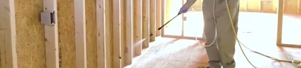 Termite treatment technician applying spray along framing and unfinished walls in Arlington, TX