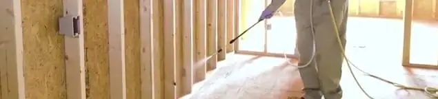 Termite treatment technician applying spray along framing and unfinished walls in Arlington, TX